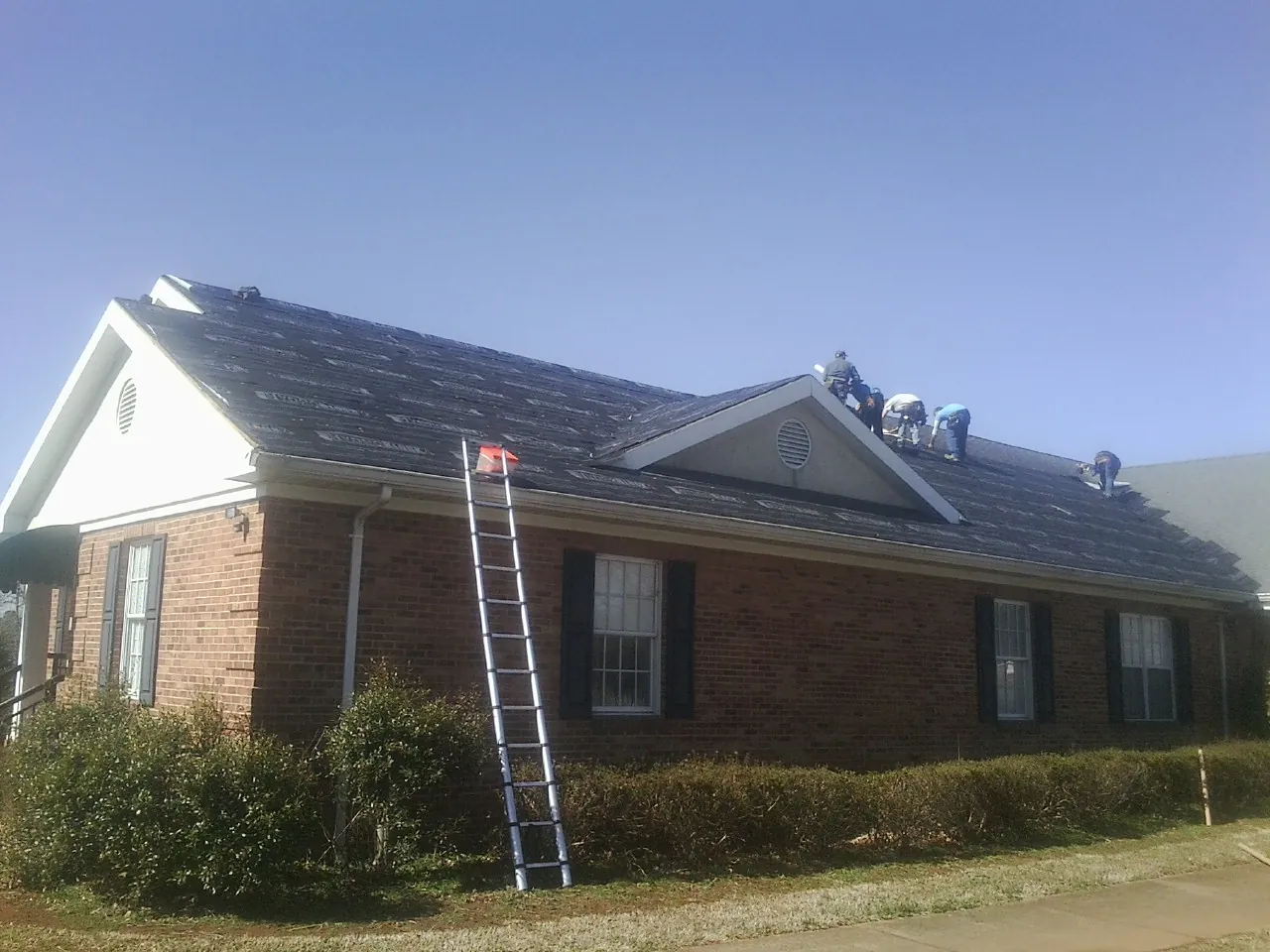 Crew tearing shingles off a brick ranch roof with a ladder set — Metal Roof Repair work by our crew in Everetts