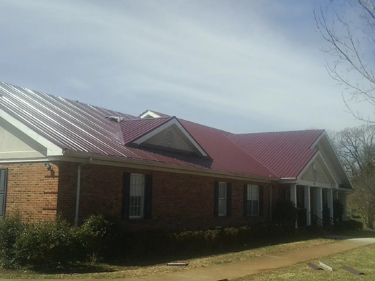 Red metal roof with gabled entries on a long brick building, from a Hail Damage Roof Repair job in Everetts