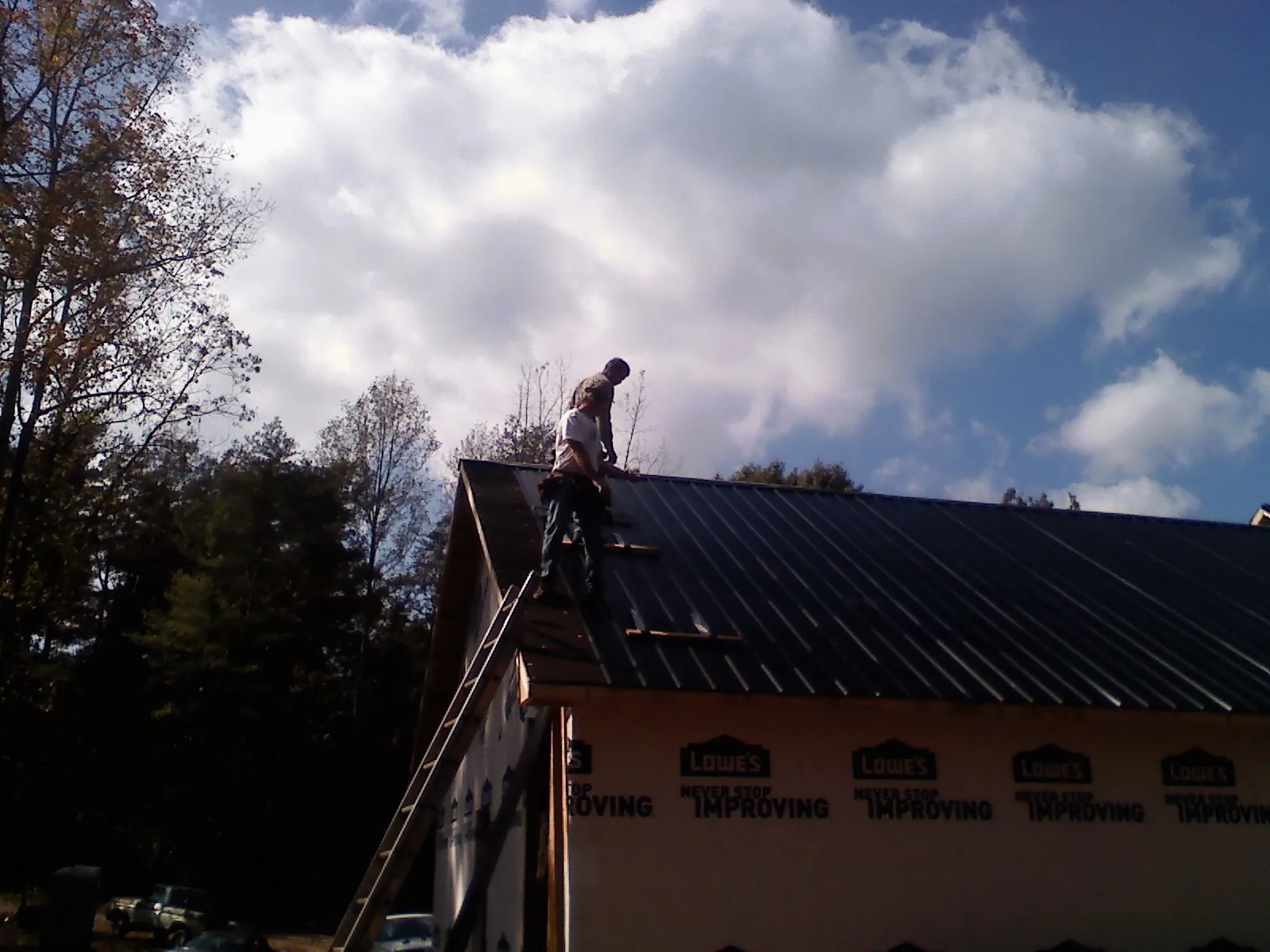 Roofer fastening dark metal panels high against a cloudy sky, from a Roof Inspection job in Everetts