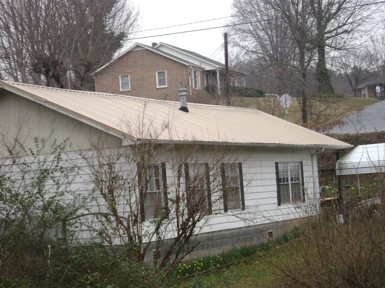 Tan metal roof on a white sided house set into a hillside — Commercial Roofing by Roofing Brothers in Everetts